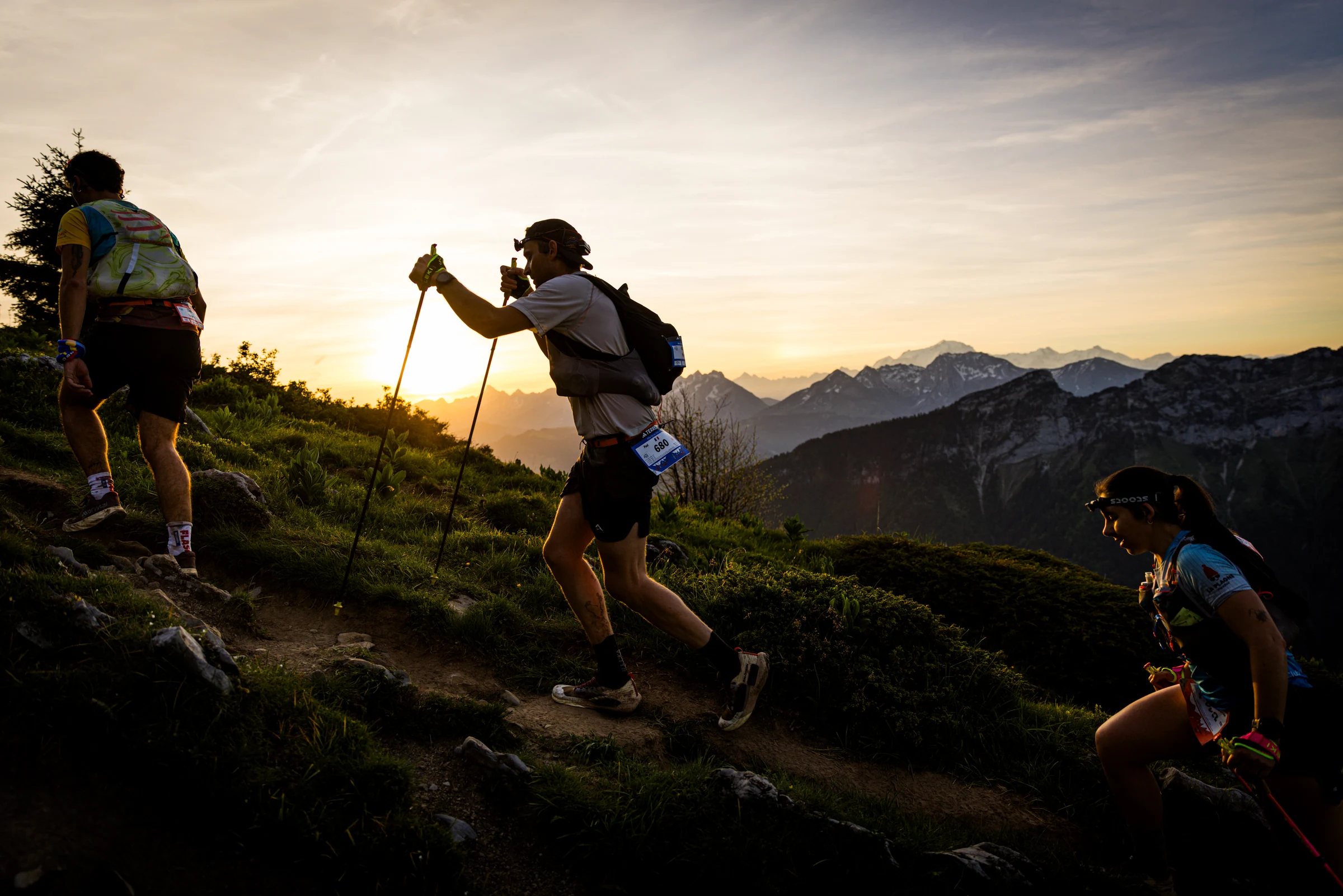 Des coureurs gravissent un sentier alpin au lever du soleil.