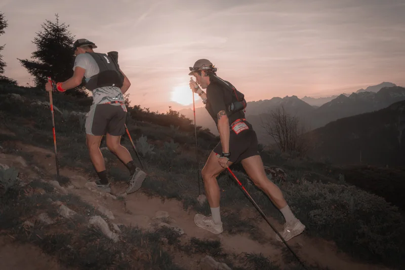 Deux coureuses progressent sur un sentier de montagne dans la lumière du matin.